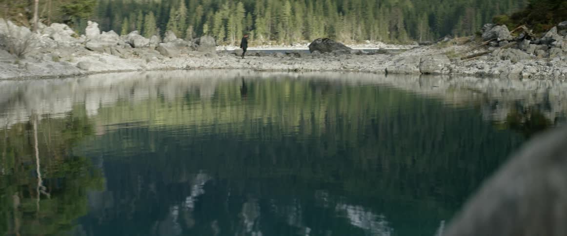 A man walks on the rocky bank of a lake