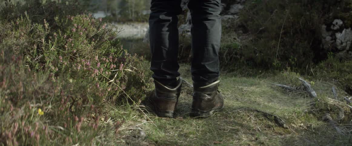 A man wearing boots stands by the water