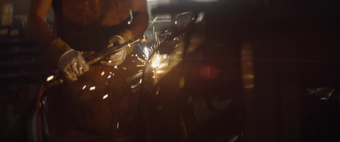 A man is welding some metal in a warehouse during the day