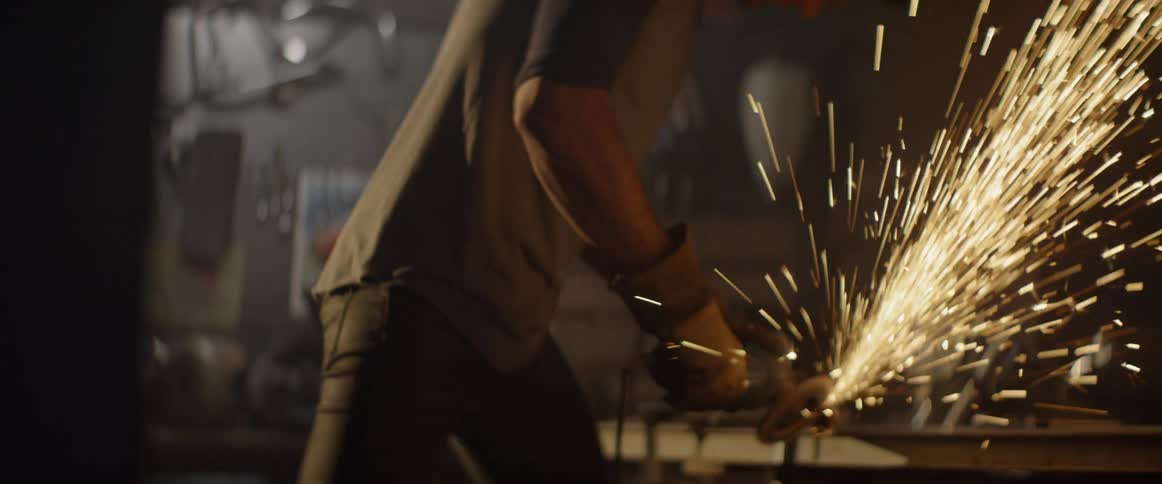 Sparks are flying from a grinder as a man uses it to cut metal