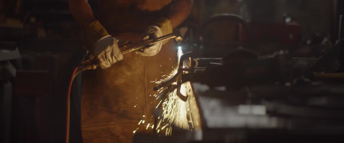 A man wearing a helmet uses a welding torch in a workshop