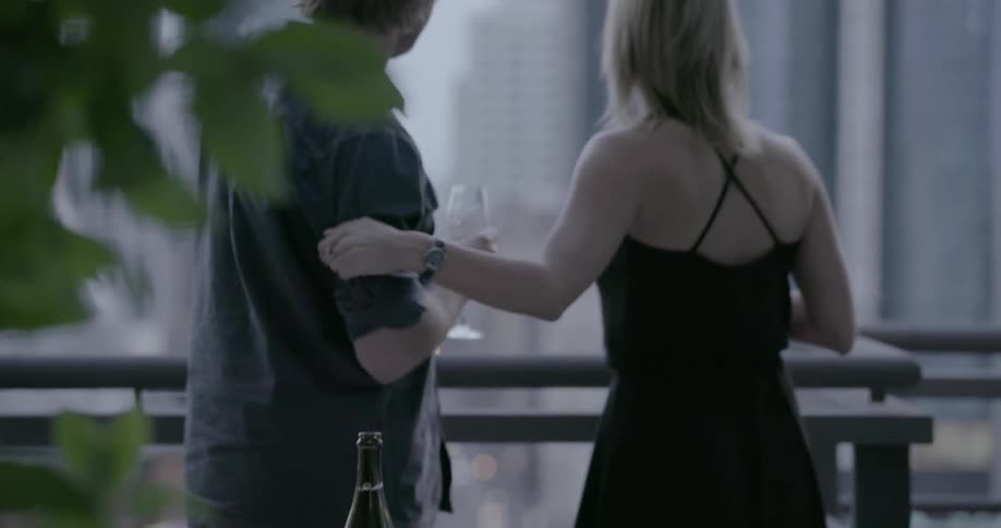 A man and woman celebrate with champagne on a balcony and embrace