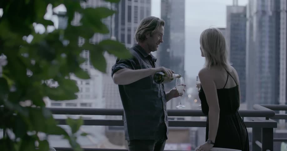 A man is pouring wine for a woman on the balcony