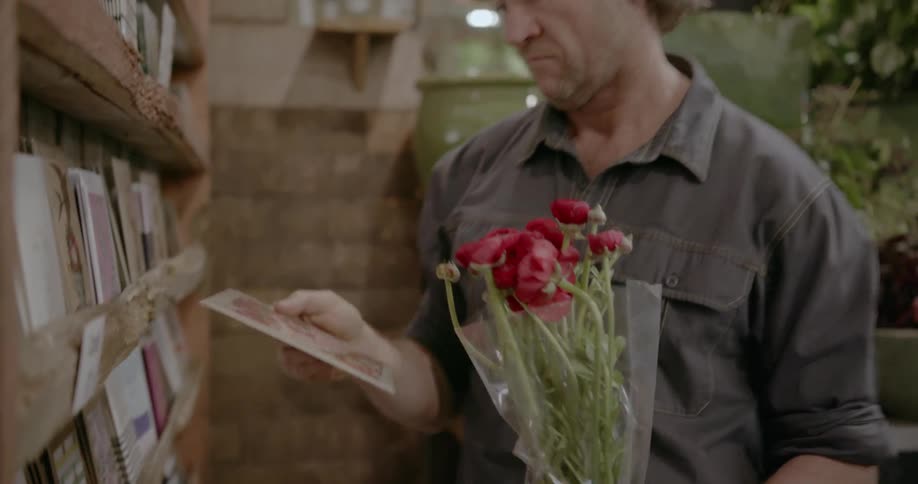 A man holding a bouquet of flowers picks up a card