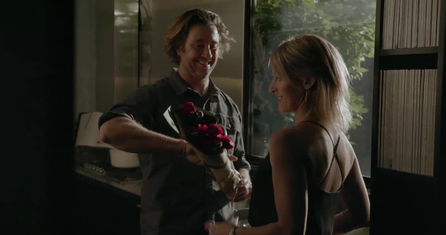 A man and woman kiss and he gives her flowers