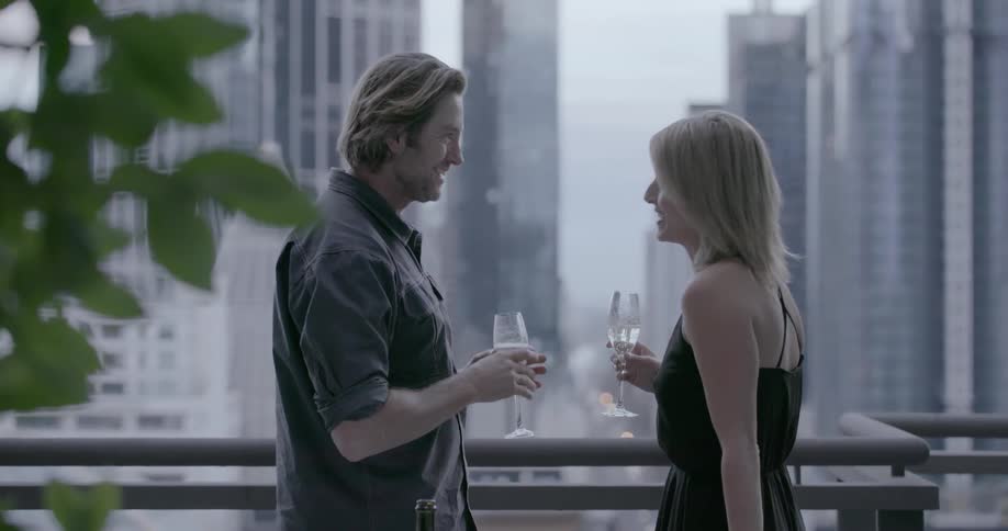 A man and woman have a toast on the balcony before hugging