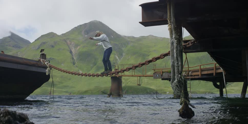 A man is balancing crossing over a chain towards a boat