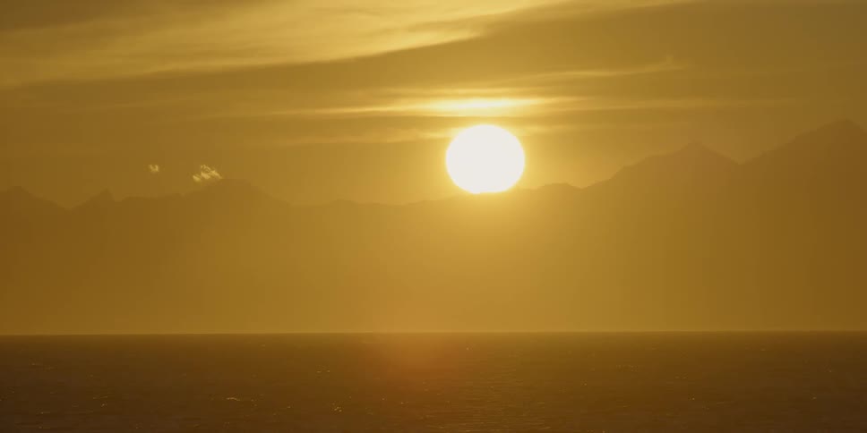 The sun begins to set behind mountains