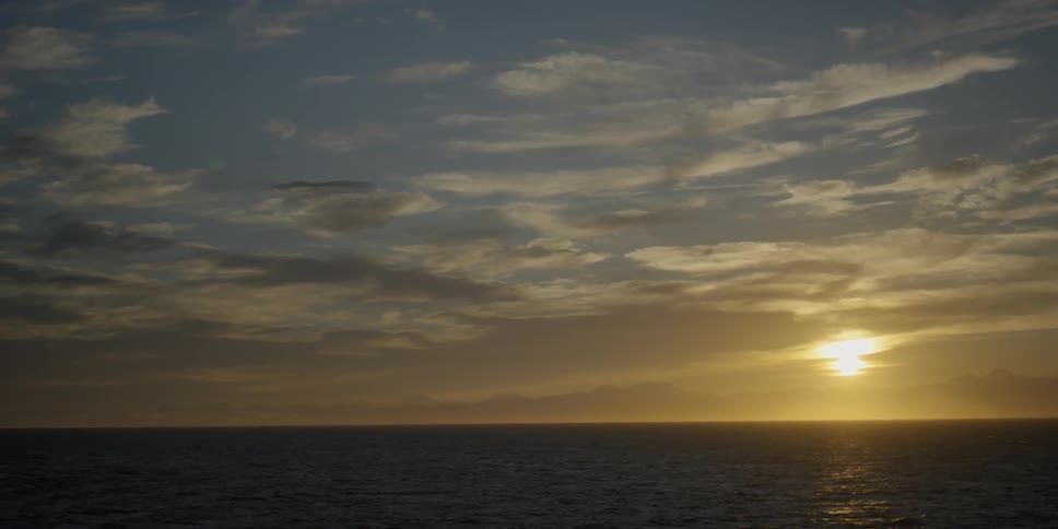 The sun is rising over coastal mountains on a cloudy day