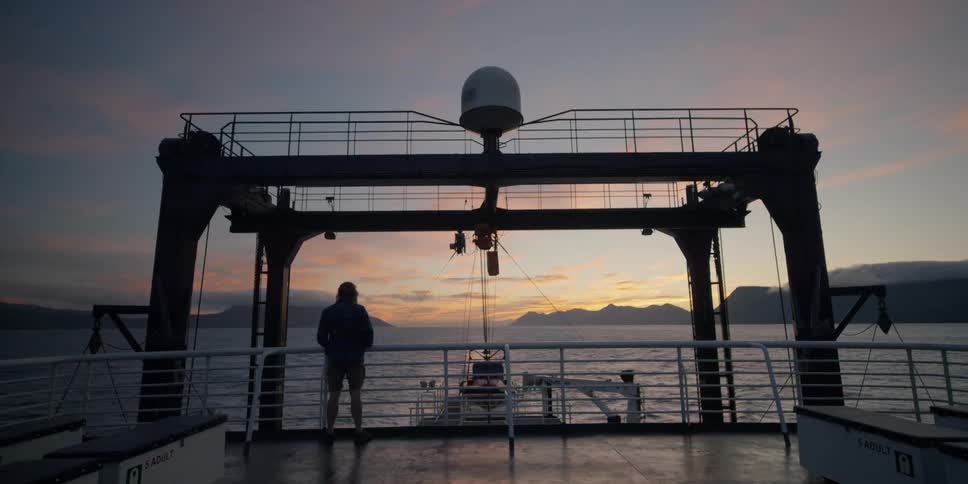 A man is standing on a boat at sunset