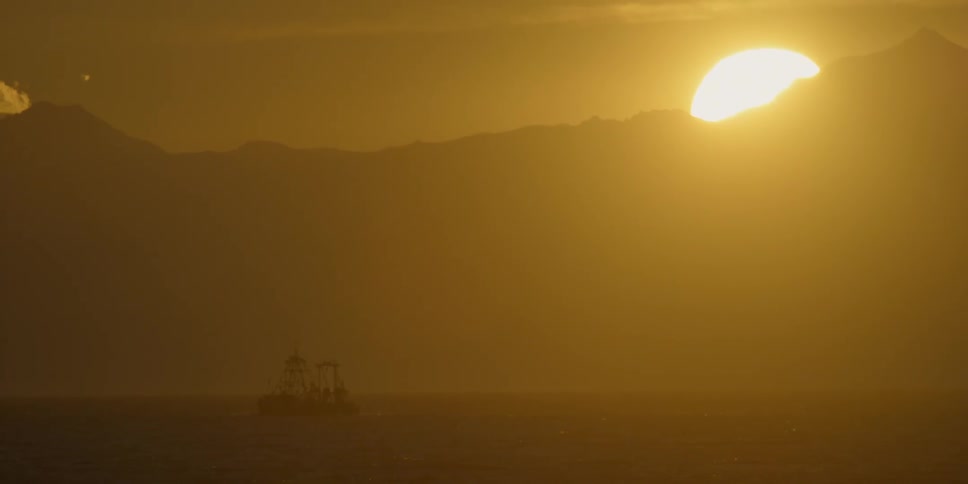A boat drifts in the water as the sun sets