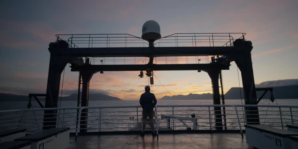 A man is standing on a boat at sunset