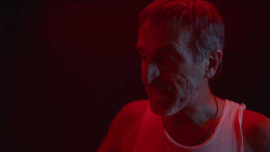 A man yells in a red lit room