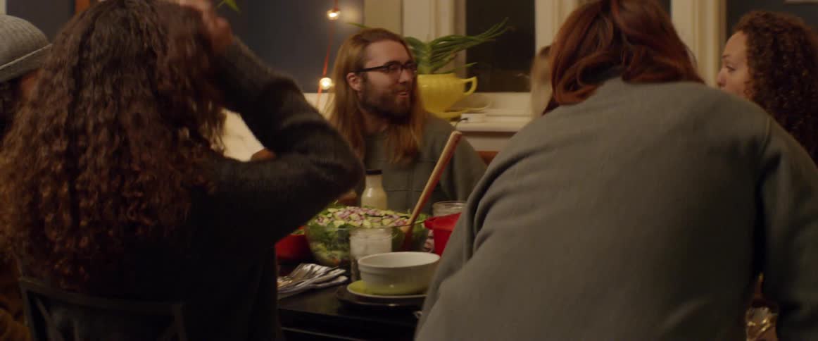 A group of friends laughs and socializes at a dinner table at night