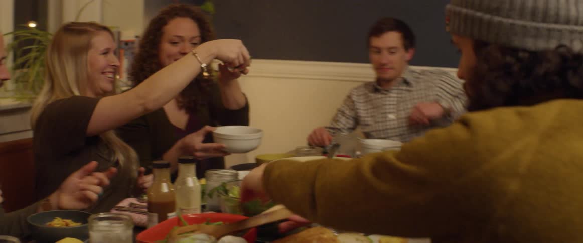 A group of friends is sharing food at a dinner table at night