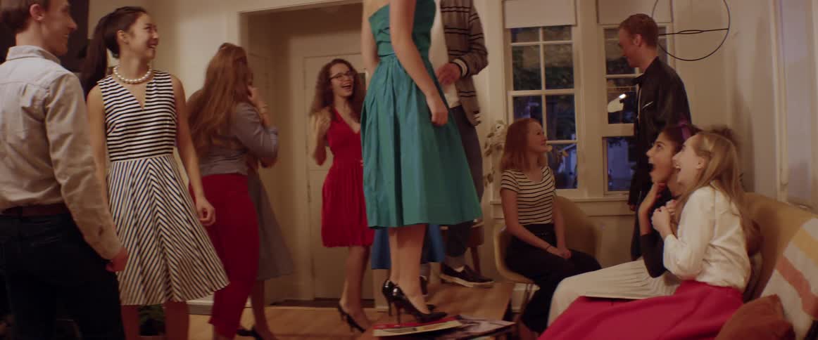 A teenage girl climbs on a table to dance at a party with her friends