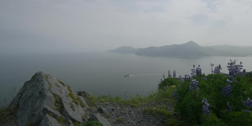 A boat travels in the water below a tall cliffside