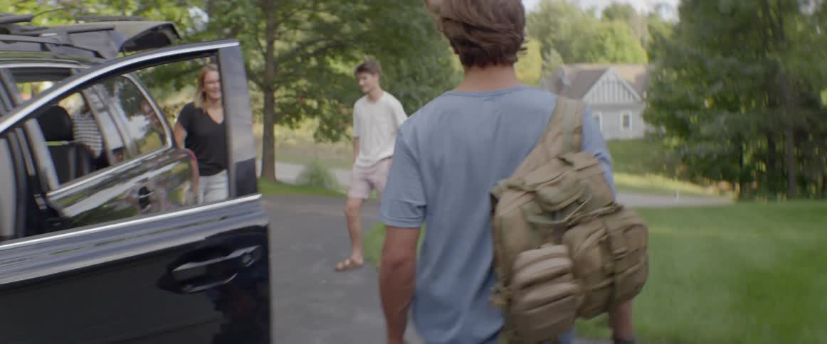 A man is packing bags into an suv as his friends and family look on
