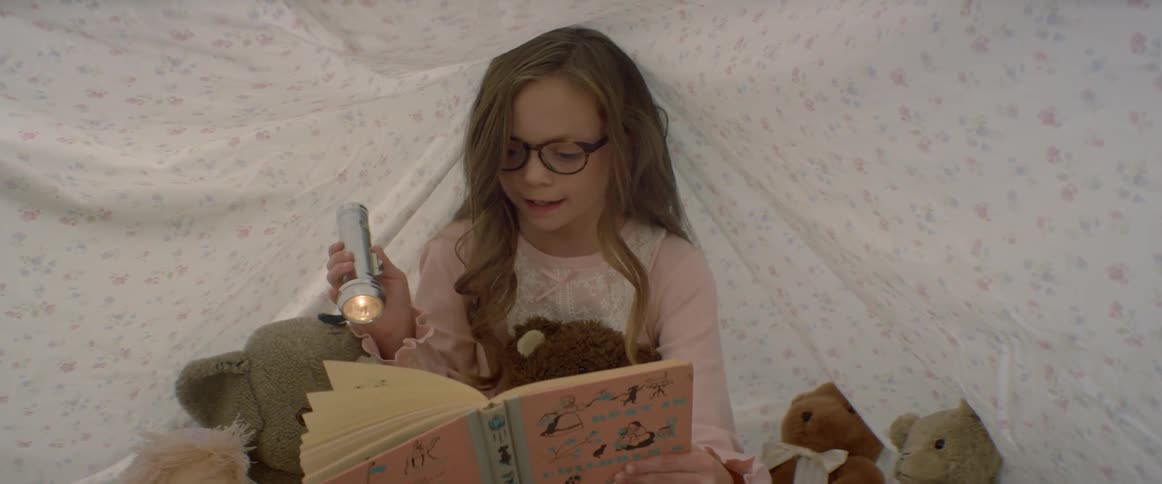 A young girl reads a book with a flashlight in a sheet fort