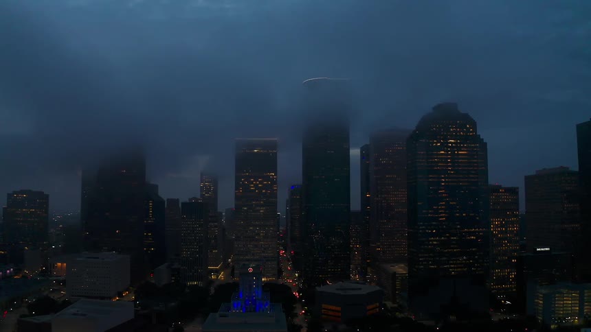 Clouds are hanging above the tops of skyscrapers in a city at dusk