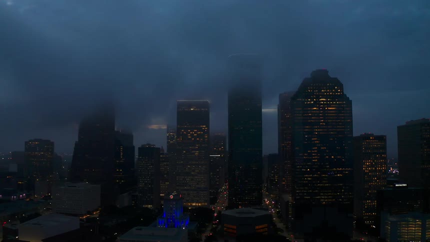 City buildings are illuminated under foggy skies