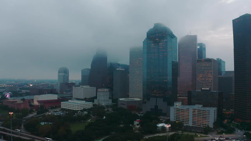 Clouds are hanging above the tops of skyscrapers in a city at dusk