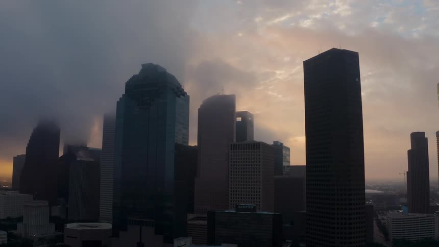 Clouds are drifting over the tops of skyscrapers in a city at dusk