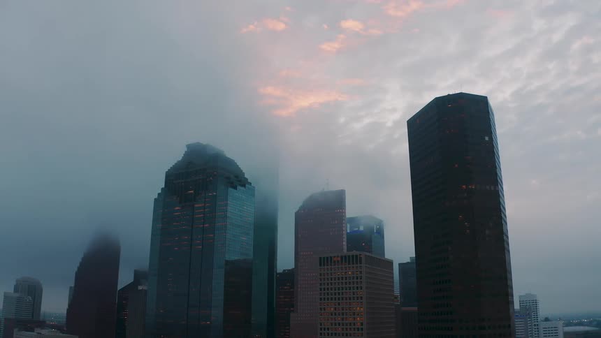 Clouds cover the tops of skyscrapers in a city at sunset