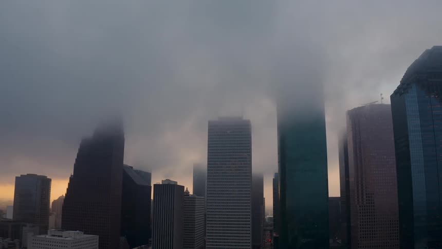 Clouds are hanging above the tops of skyscrapers in a city at dusk