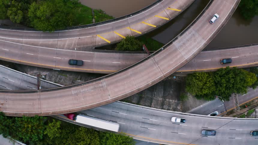 Vehicles are traveling on a freeway system above a river during the day