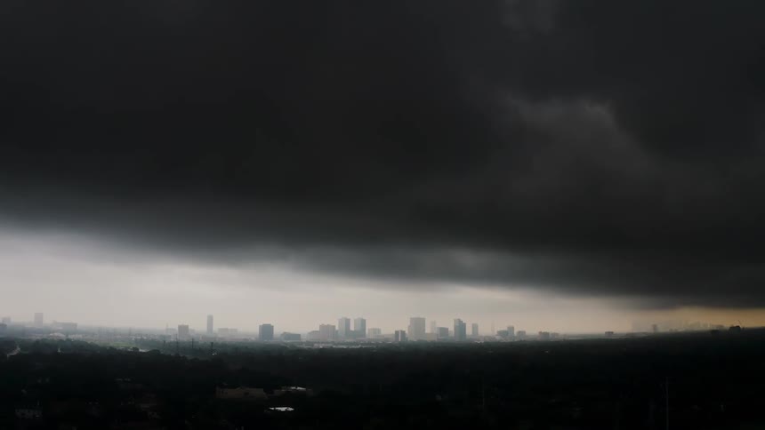 Storm clouds are moving across a city at dusk