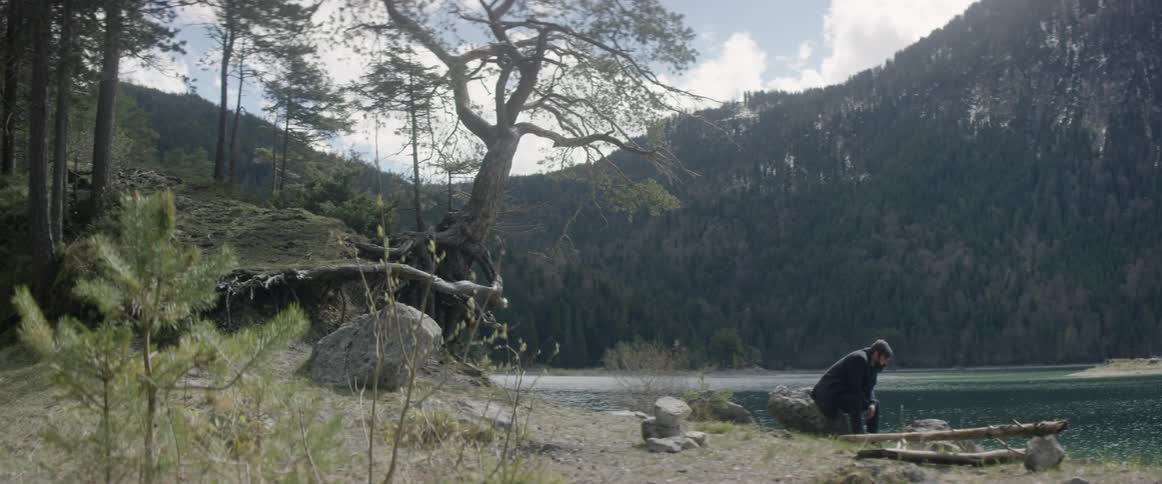A man sits on a rock next to the water