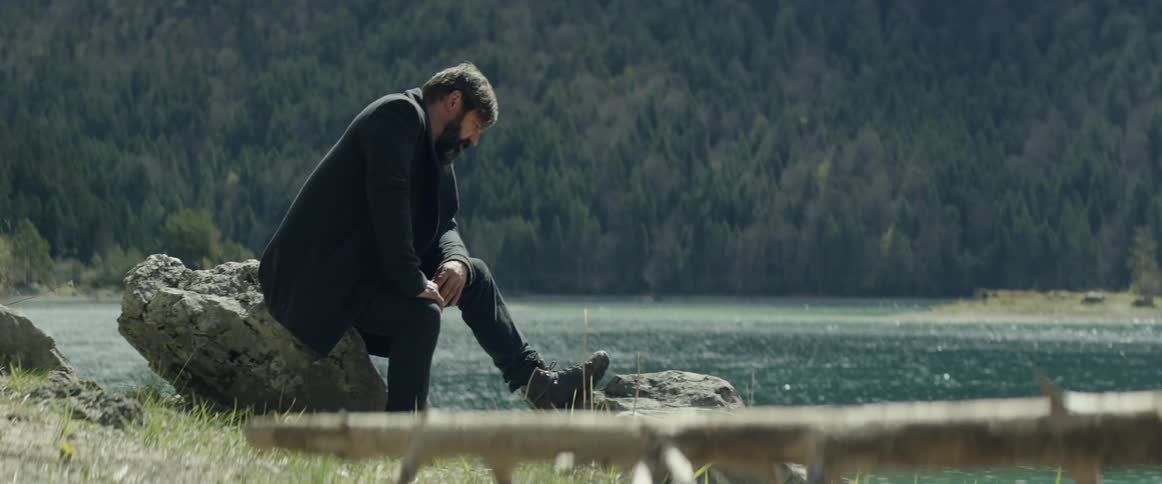 A man sits on a rock by the lake shore