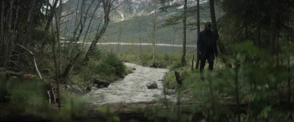 A man is walking near a creek in a natural setting on a cold day