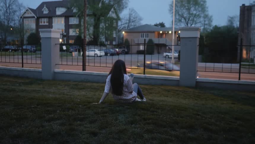 Teenage girl sits on a lawn with her phone at dusk