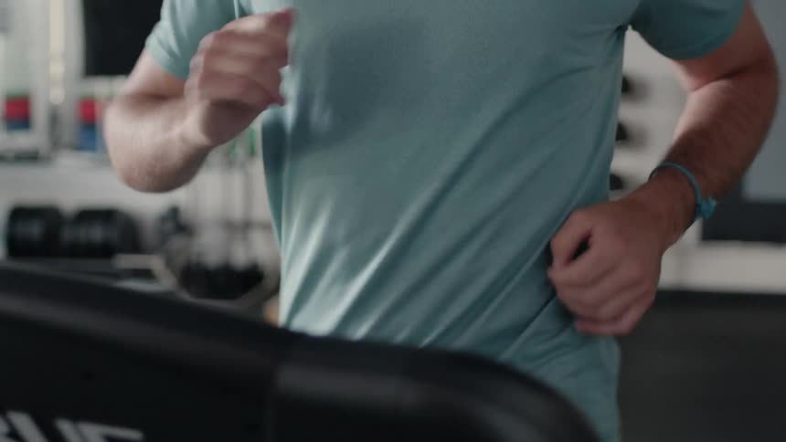 A man is jogging on a treadmill in a gym during the day