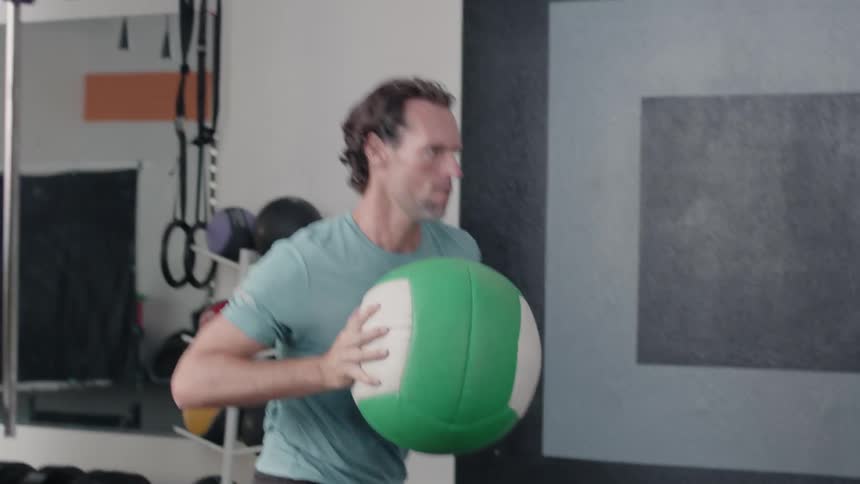 A man is throwing a weight ball at a wall and catching it