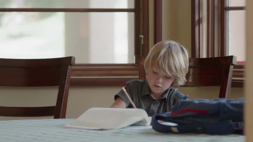 A man is bringing a snack to a boy sitting at a table doing homework during the day