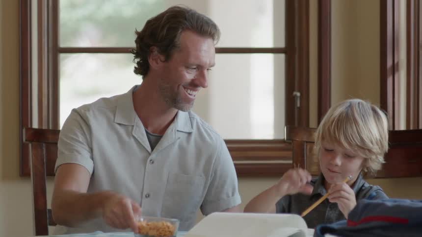 A man hands some food over to a child doing homework
