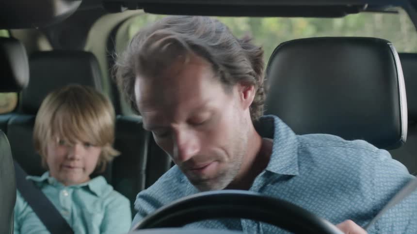 Man buckles up in the driver's seat of a car with a boy in the backseat