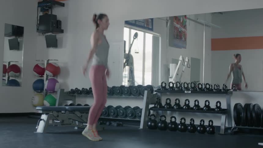 A woman does jumping jacks in a gym