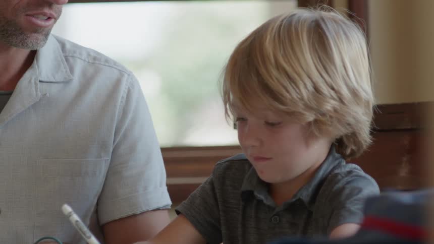 A man sits with a young boy as he draws with markers