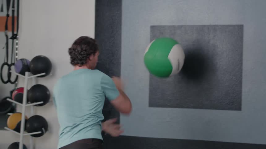 A man is throwing a weight ball against a wall in a gym during the day