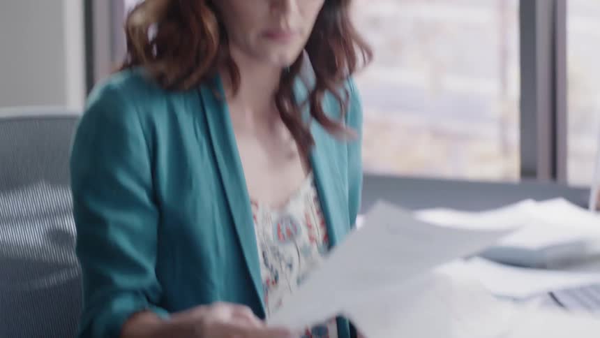 A woman sits at a desk and puts on her glasses to review papers