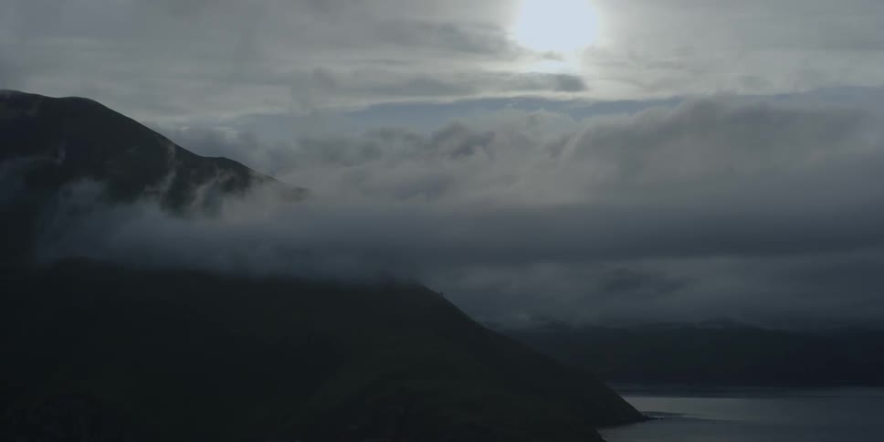 Clouds roll over mountains with the sun shining through