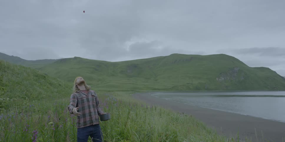A man throws a berry up in the air and catches it in his mouth