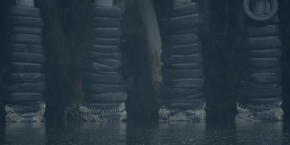 Stacks of tires on pier poles near ocean on a rainy day