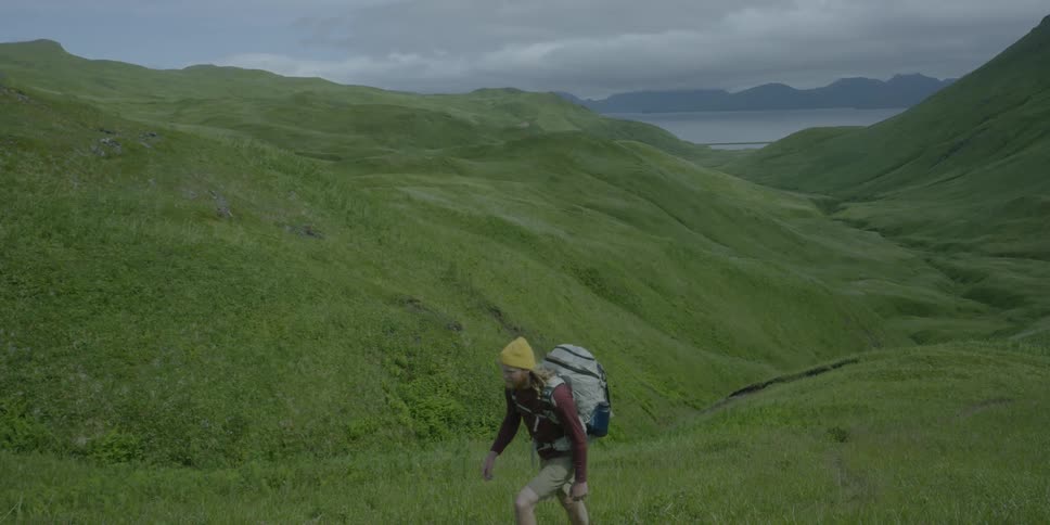 A hiker climbs up a grass covered hill