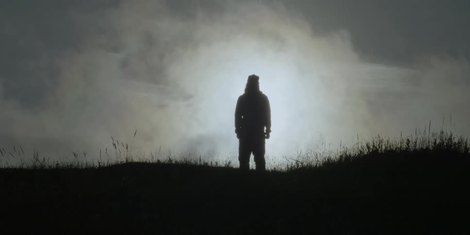 Man stands silhouetted in a grassy field