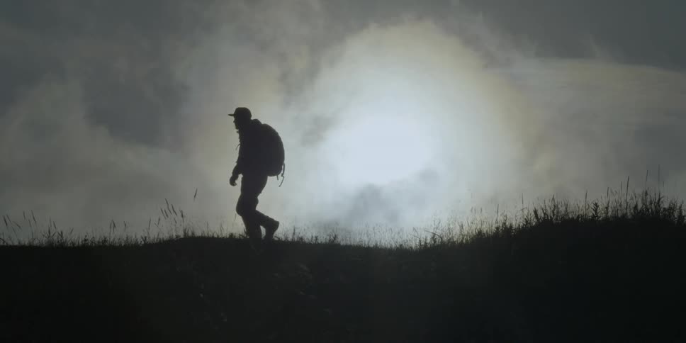 Man in silhouette walking across a grassy field